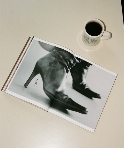 Open book with photo of a person standing under a shoe on a beige surface next to a cup of coffee.