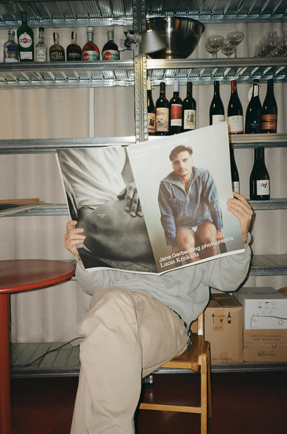 Person holding a magazine with a man on the cover in a room with shelves and bottles.